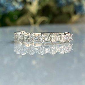 Close-up of a diamond-studded ring resting on a reflective surface with a blurred outdoor background in green and blue hues.