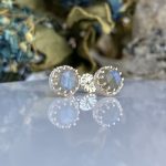 Pair of silver stud earrings with pale blue faceted stones set in a beaded bezel on a reflective surface.