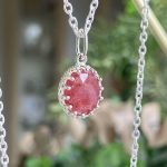 Oval pink faceted gemstone pendant in a detailed silver bezel on a thin chain, close-up.