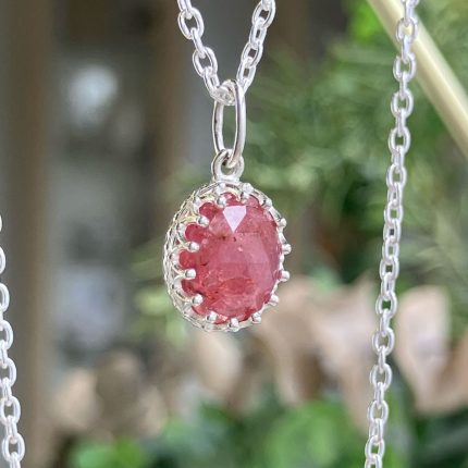 Oval pink faceted gemstone pendant in a detailed silver bezel on a thin chain, close-up.