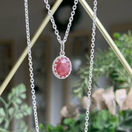 Oval pink gemstone pendant in a silver bezel setting hanging from a delicate silver chain.