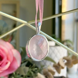 Oval pale pink faceted gemstone pendant in a silver setting hanging from a pink ribbon.
