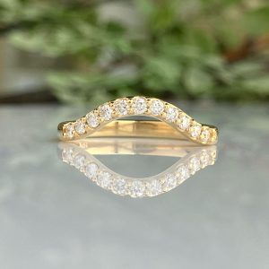 Gold curved diamond band ring with alternating round-cut stones, resting on a reflective surface.