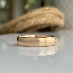 Rose gold wedding band resting on a reflective surface with a softly blurred background.