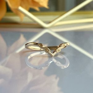 Gold V-shaped ring with spiral engravings on a reflective surface.