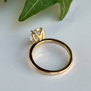 Gold ring with a prong-set diamond on a plain white surface, seen from the side.