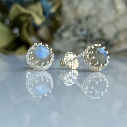 Silver stud earrings with square-cut blue gemstones in an ornate silver halo, reflected on a glossy surface.