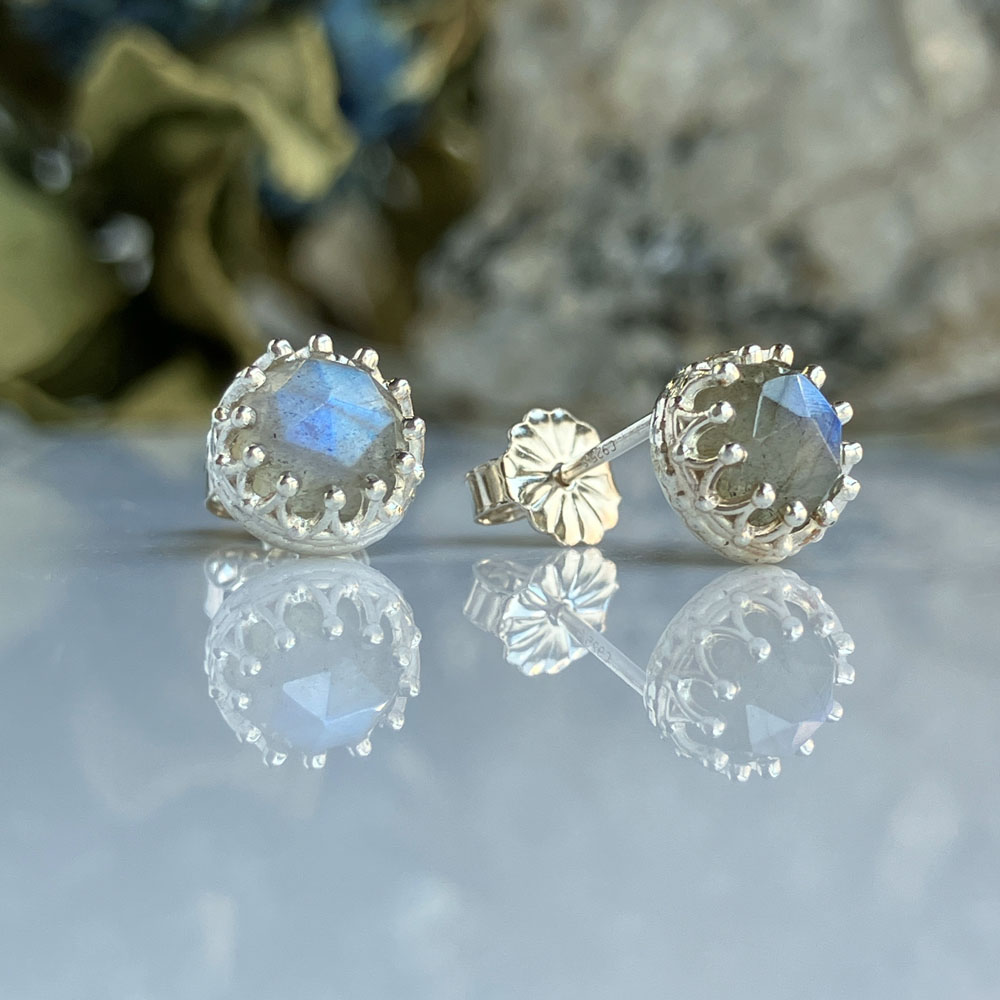 sterling silver labradorite earringsjpeg | Posy Fine Jewellery Toronto Silver stud earrings with square-cut blue gemstones in an ornate silver halo, reflected on a glossy surface.