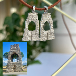 Two silver-tone arch-shaped ruin charms hanging from a brown cord; inset shows a real ancient stone arch ruin in a field under a blue sky.