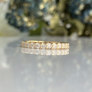 Gold band with a row of diamonds resting on a reflective surface.