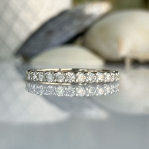 Pavé diamond eternity ring in white metal on a reflective surface with a softly blurred background.