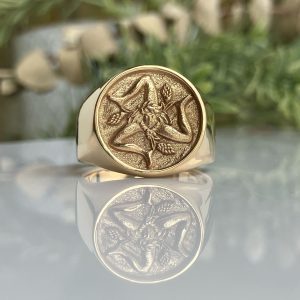Close-up of a gold coin with an eagle design, mounted in a ring, against a blurred outdoor background.