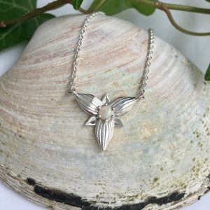 Silver necklace with a winged, flower-like pendant featuring a central opal on a textured shell background.