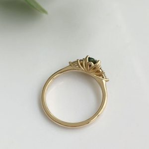 Gold ring with a green gemstone set in an ornate floral filigree setting on a light background, close-up.