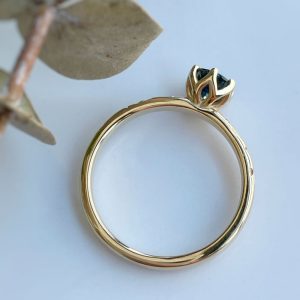 Gold ring with a small dark blue gemstone in a flower/crown-style setting on a light background.
