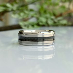 Close-up of a silver ring with a dark carbon-fiber center inlay on a glossy surface.