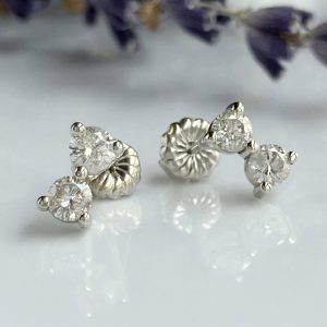 Silver stud earrings with multiple clear diamonds in prong settings, resting on a reflective surface.