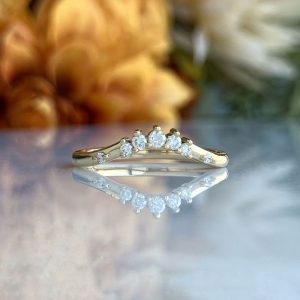 Gold ring with five diamonds set in a curved arc, reflected on a glossy surface.