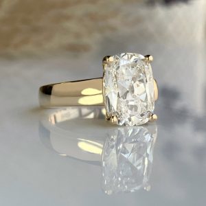 Gold ring with a rectangular cushion-cut diamond held by four prongs, on a reflective surface.