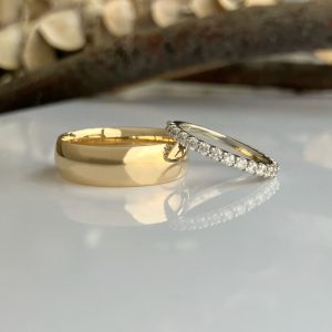 Gold wedding band beside a diamond-studded eternity ring on a reflective white surface.