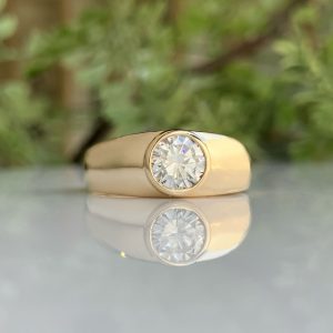 Gold ring with a large diamond on a reflective surface, softly blurred green background behind it.