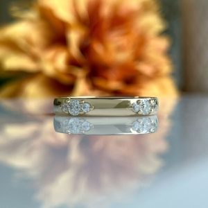 Gold gold-band ring with diamond clusters on the sides, shown with a mirrored reflection on a glossy surface.
