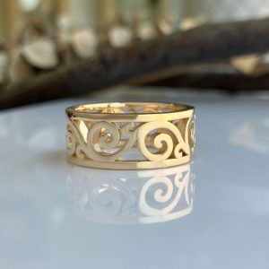 Gold filigree ring with swirling scrollwork on a reflective surface.