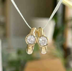 Pair of gold, round-diamond pendants hanging from a white cord necklace, close-up image of two matching jewelry pieces