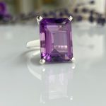 Emerald-cut purple amethyst ring set in a silver band with a reflective surface beneath.