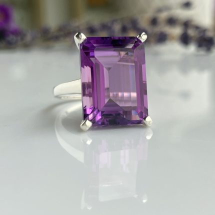 Emerald-cut purple amethyst ring set in a silver band with a reflective surface beneath.