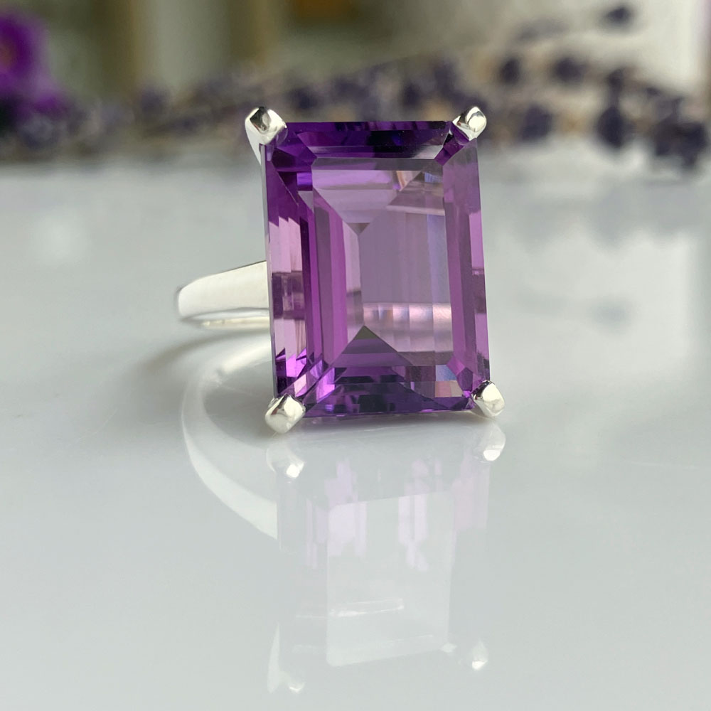 amethyst cocktail ringjpeg | Posy Fine Jewellery Toronto Emerald-cut purple amethyst ring set in a silver band with a reflective surface beneath.