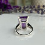 Silver ring with three square-cut purple amethyst stones in a modern vertical setting on a white, reflective surface.