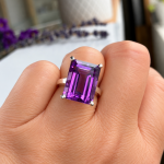 Emerald-cut purple amethyst ring with four prongs worn on a finger.