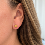 Close-up of a woman's ear wearing a small gold stud with a yellow gemstone.