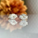 Silver stud earrings with a scalloped flower back and wrapped ribbon design, reflected on a glass surface with autumnal background.