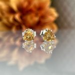 Pair of yellow gemstone stud earrings with silver prongs placed on a reflective surface.