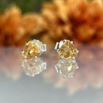 Pair of yellow gemstone stud earrings with silver prong settings on a reflective surface.