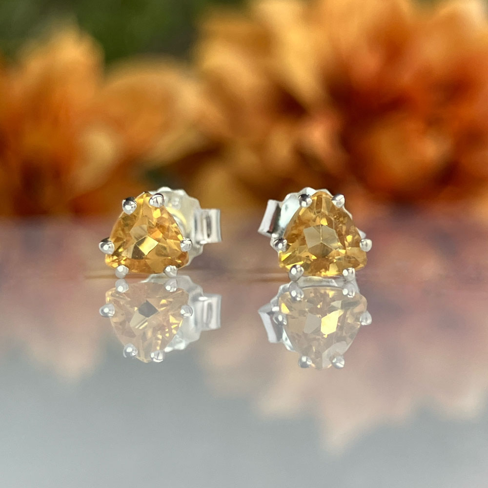 trillion cut citrine birthstone earringsjpeg | Posy Fine Jewellery Toronto Pair of yellow gemstone stud earrings with silver prong settings on a reflective surface.